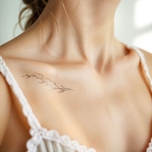 A close-up of a woman's chest is shown, revealing a tattoo of a plant. The woman has long, flowing hair and is wearing a necklace that drapes down her neck - Wide Awake NYC 