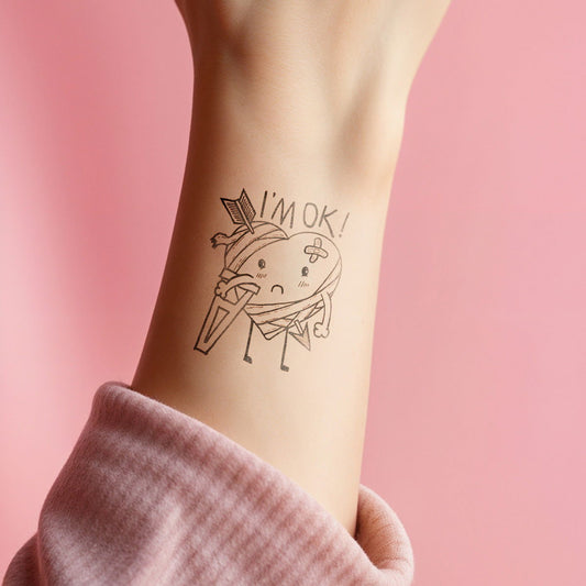 A close-up of a woman's forearm wearing a pink sweaters and heart tattoo said "I'm ok", pink background - Wide Awake NYC 