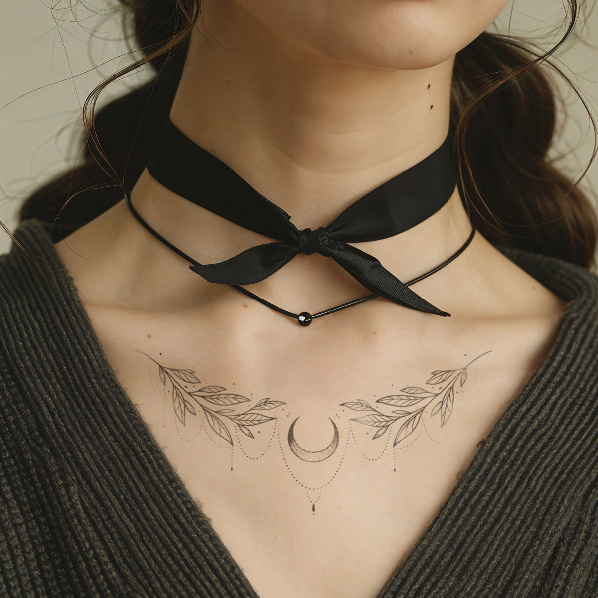 A close-up of a woman's neck with a chokker and a tattoo showing vines and a moon, grey background - Wide Awake NYC
