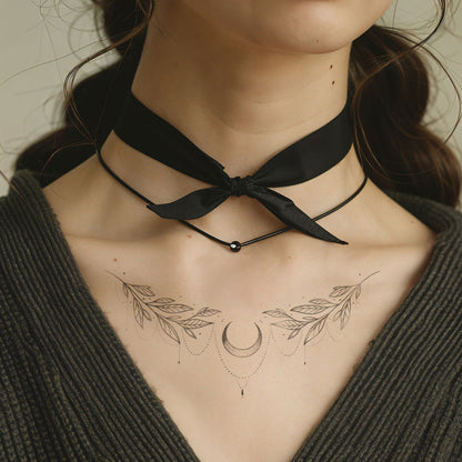 A close-up of a woman's neck with a chokker and a tattoo showing vines and a moon, grey background - Wide Awake NYC
