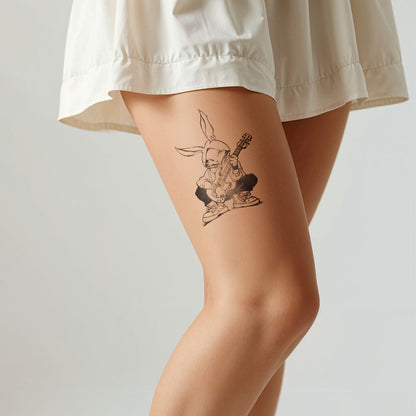 A women's leg wearing a white skirt with a tattoo showing rabbit with a guitar sitting with street style, on a white background - Wide Awake NY