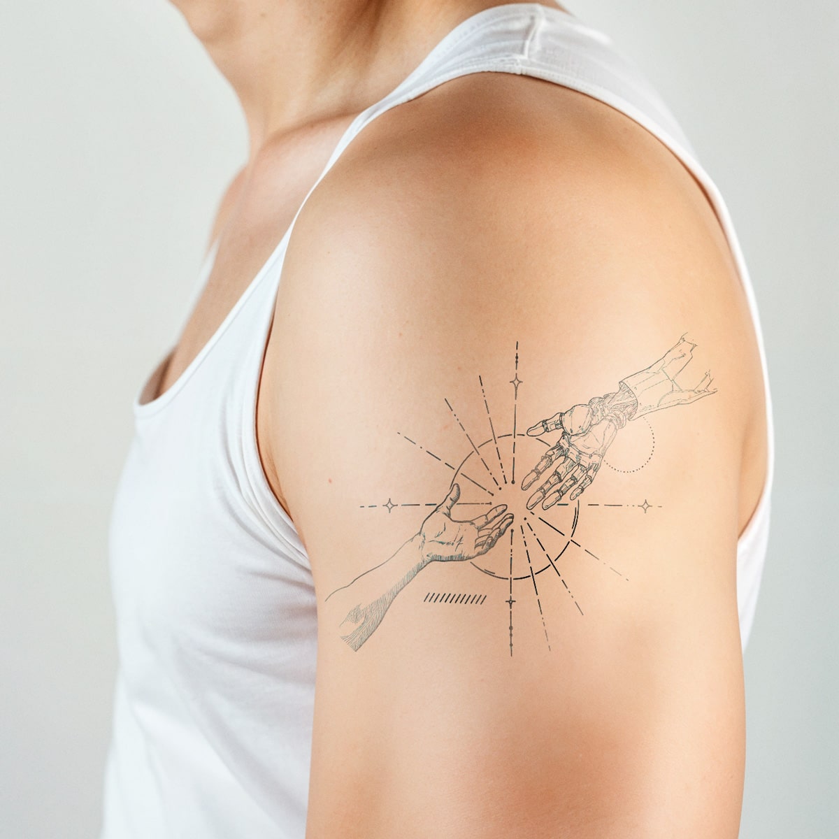 The Creation of Human tattoo shows a human hand reach to a robot hand with some star around them on a man's arm wearing a white tank in a white background - Wide Awake NYC 