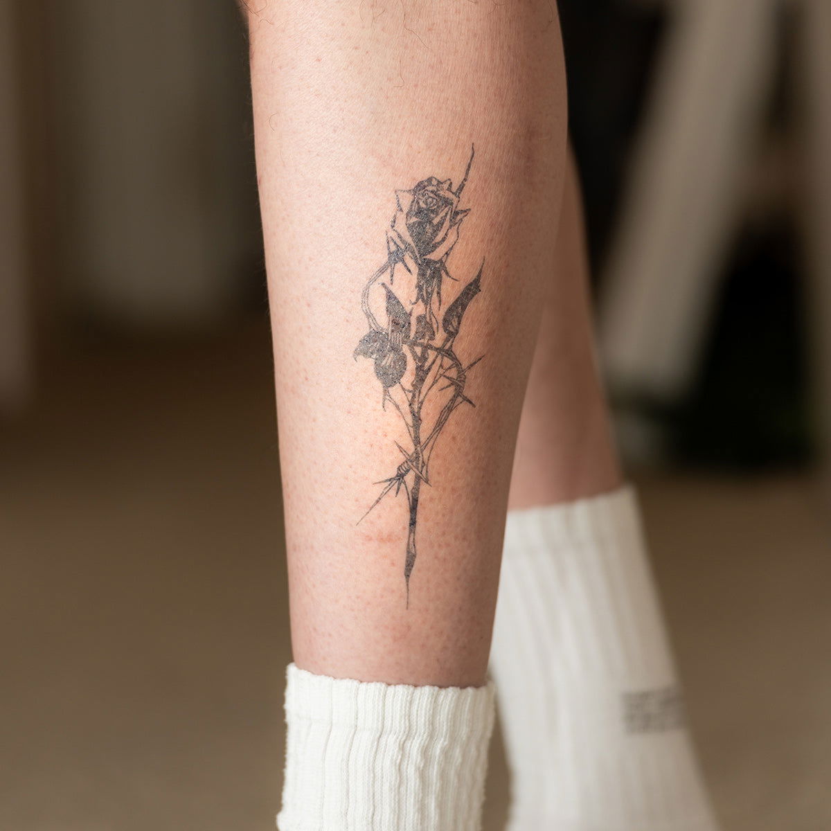 A rose tattoo on a man's leg in a room - Wide Awake NYC